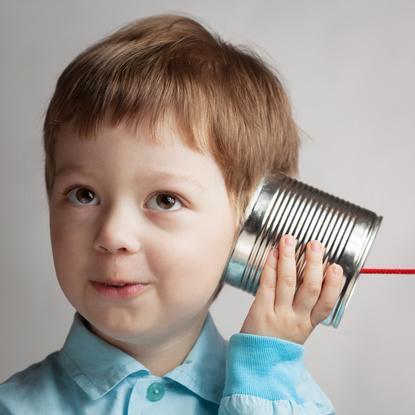 Ein Kind hält sich eine Blechdose an sein Ohr.
